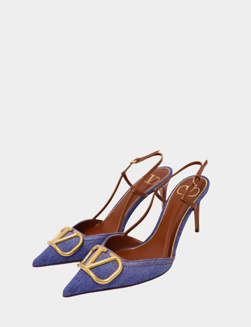 Valentino slingback heels in blue denim with pointed toe, gold V-logo hardware, and slim stiletto heel on a plain background.