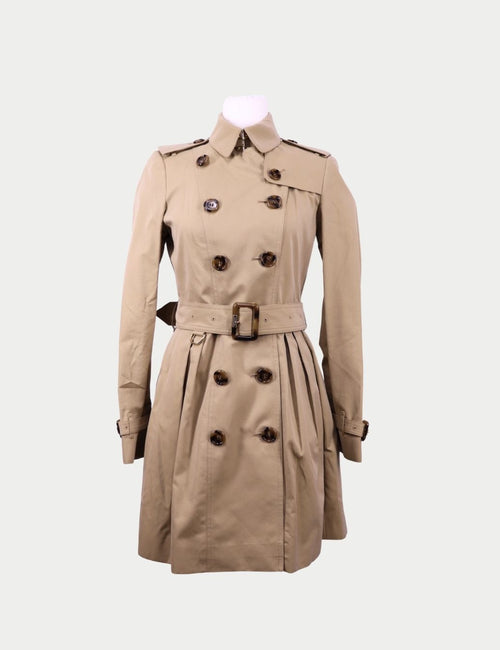Beige Burberry double-breasted trench coat with waist belt, shoulder epaulettes, pleated skirt detail, and long sleeves