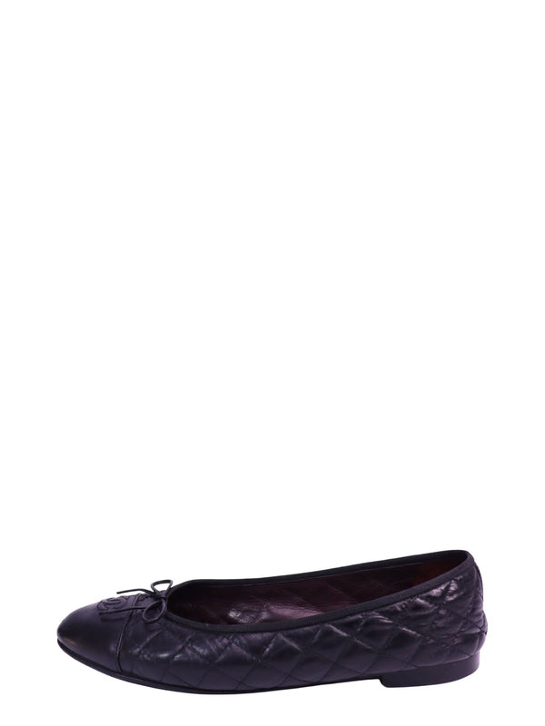 Black Chanel quilted lambskin ballet flats featuring a cap-toe design, signature interlocking CC logo detail on the toe, bow accent, leather lining, and flat sole. Classic slip-on silhouette with diamond quilting throughout the upper