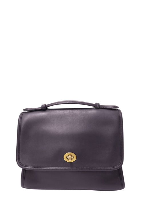 Coach black leather flap satchel handbag with gold-tone turn-lock closure, slim top handle and structured rectangular silhouette
