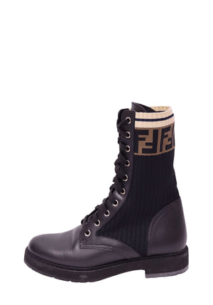 Fendi black leather lace-up combat boot featuring ribbed black knit shaft, brown FF monogram logo, cream striped cuff, silver-tone eyelets, and chunky rubber sole