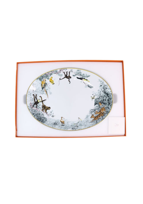 Hermès Carnets d'Équateur porcelain oval serving platter featuring detailed illustrations of exotic birds, monkeys, deer, and tropical foliage around the border, finished with a gold rim