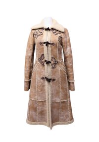 Prada beige long coat featuring cream shearling-style collar, decorative embroidered appliqués, brown toggle closures and paneled construction.