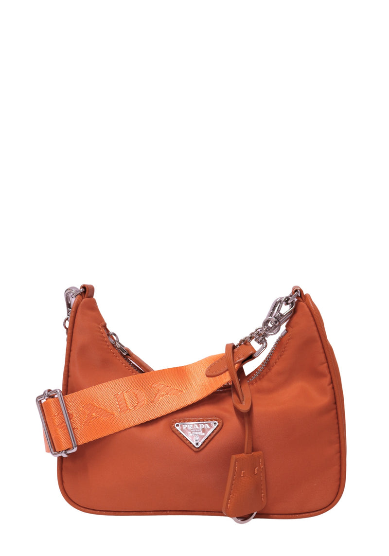 Prada burnt-orange nylon shoulder bag featuring a silver-tone triangle logo plaque, curved silhouette, top zipper, adjustable orange PRADA logo strap and matching hanging clochette.
