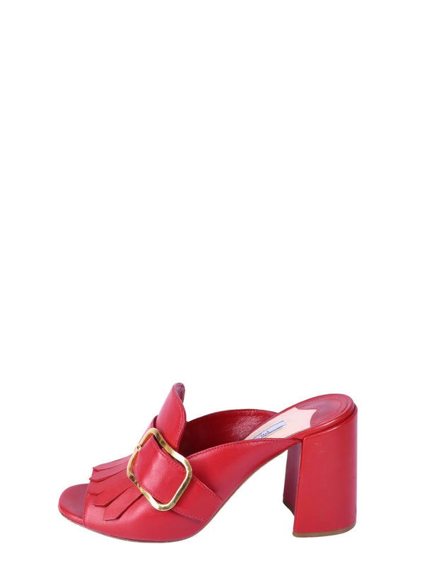 Prada red leather mule heels with fringe detailing, oversized gold-tone buckle accents, and block heels.