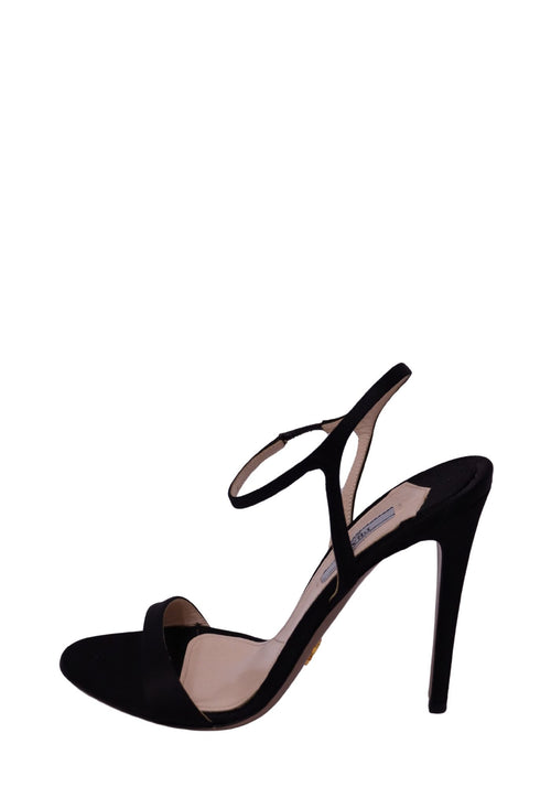 Prada black suede high-heel sandal featuring a minimalist open-toe front strap, delicate ankle strap, sculptural slingback-style detailing, nude insole, and slender black stiletto heel