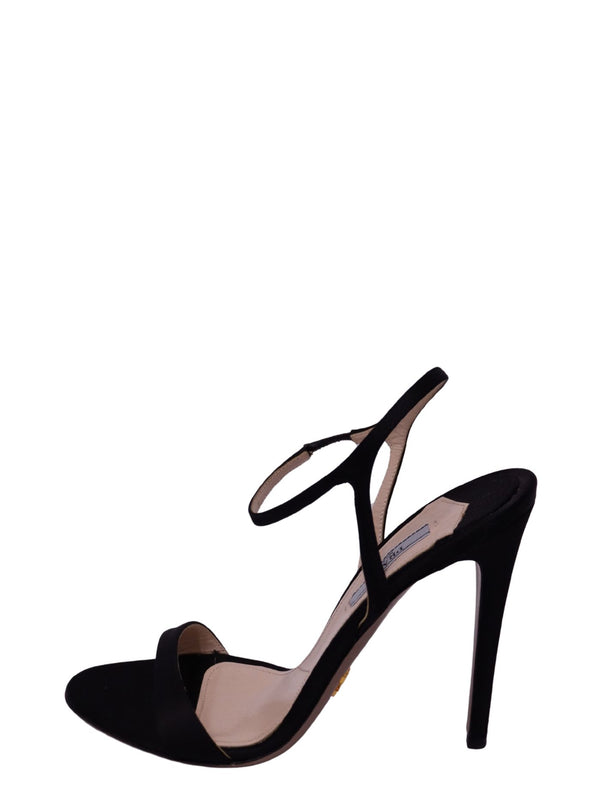 Prada black suede high-heel sandal featuring a minimalist open-toe front strap, delicate ankle strap, sculptural slingback-style detailing, nude insole, and slender black stiletto heel