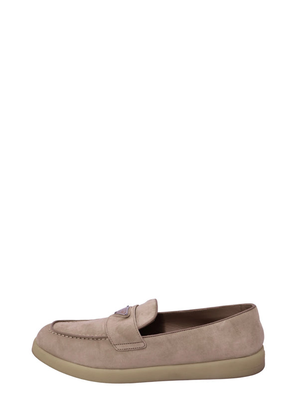 Prada beige suede penny loafer featuring a rounded moccasin-style toe, signature triangular Prada logo plaque, wide suede front strap, and tonal beige rubber sole