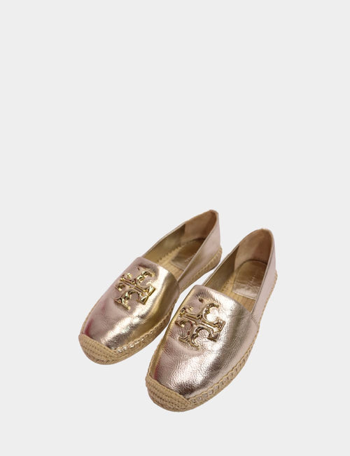 "Tory Burch metallic gold espadrilles with gold double-T logo and jute sole, displayed on white background."

