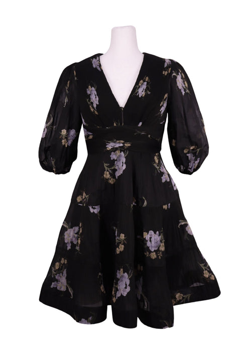 Authentic Zimmermann black floral mini dress with lilac floral print, deep V-neckline, voluminous sleeves, and pleated flowing skirt.